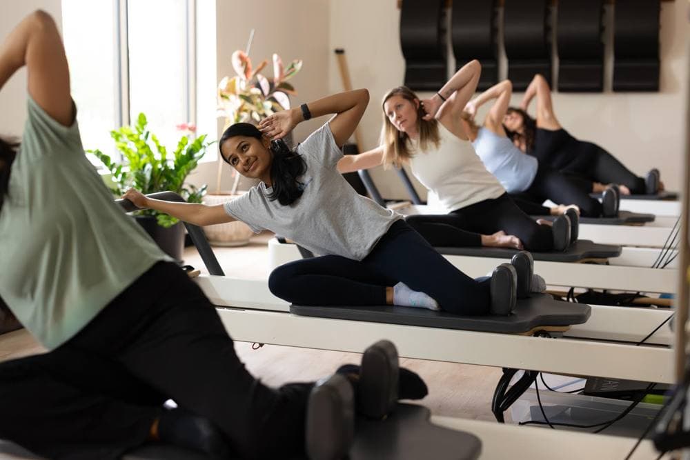 A pilates instructor guiding a client on a reformer in a bright room